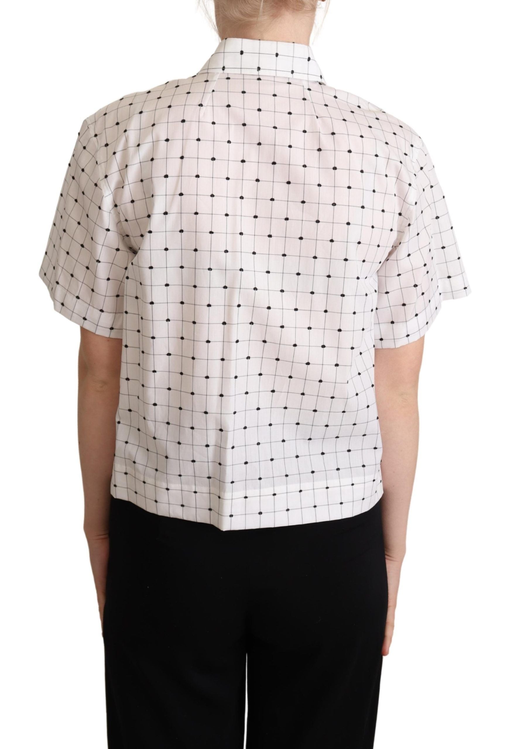 White cotton collared shirt top with black polka dots by Dolce & Gabbana, shown hanging on a wooden hanger.