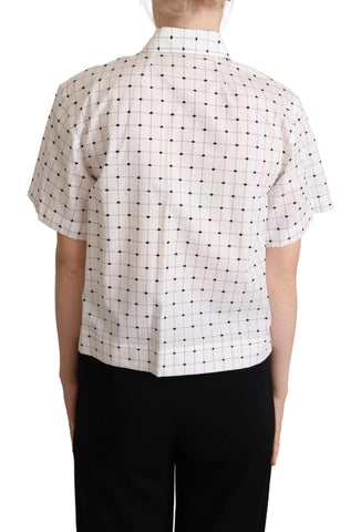 White cotton collared shirt top with black polka dots by Dolce & Gabbana, shown hanging on a wooden hanger.