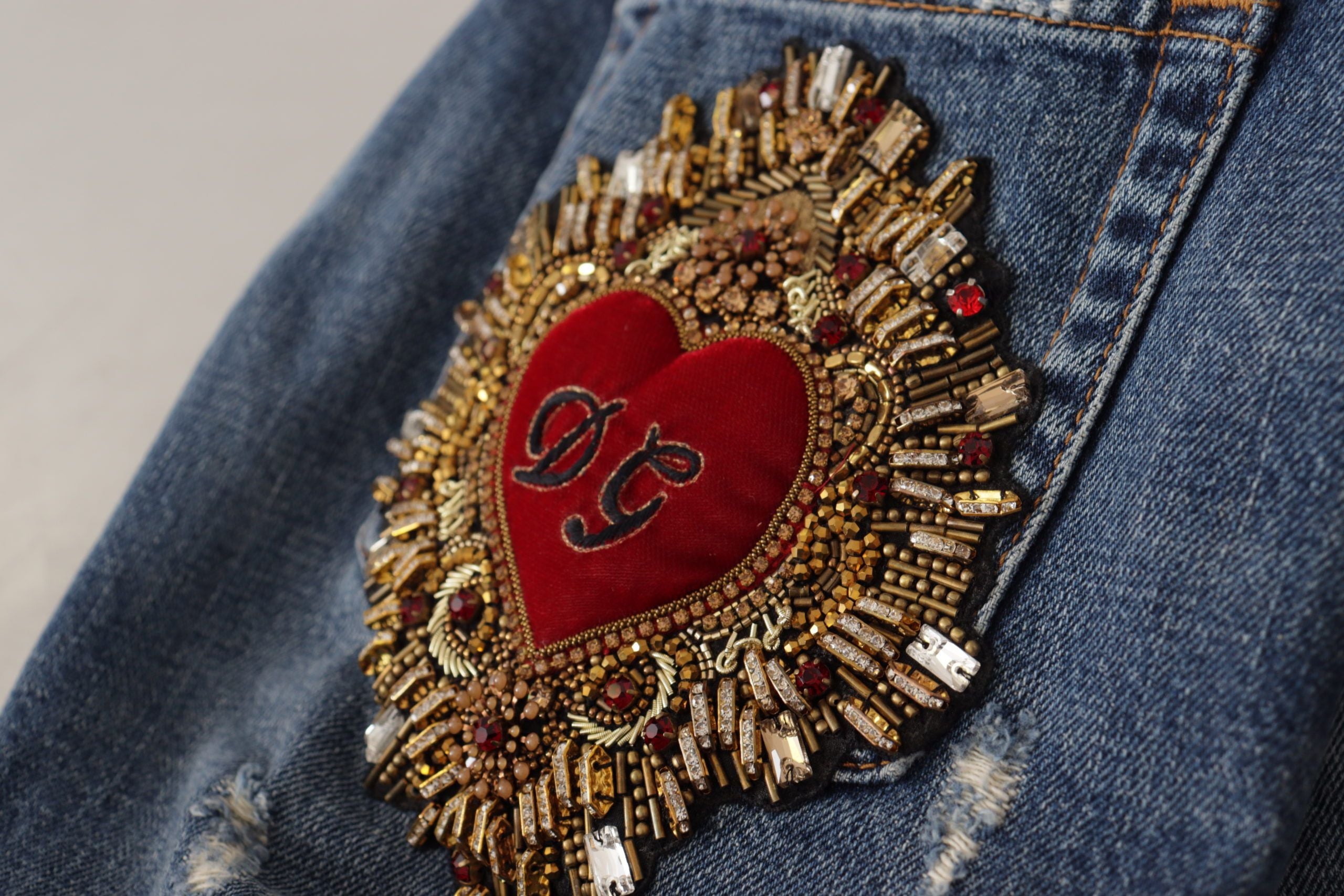 Blue denim Dolce & Gabbana jeans with Baroque heart logo patch, stylish casual pants with intricate embroidery details.