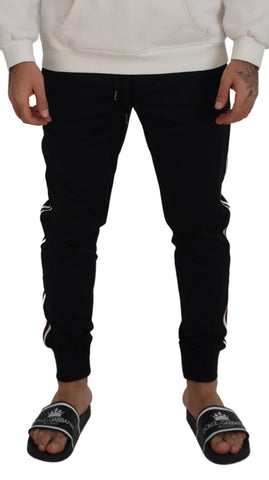 Black Dolce & Gabbana men's jogger pants with DG print, featuring a relaxed fit and elastic waistband, shown on a hanger.