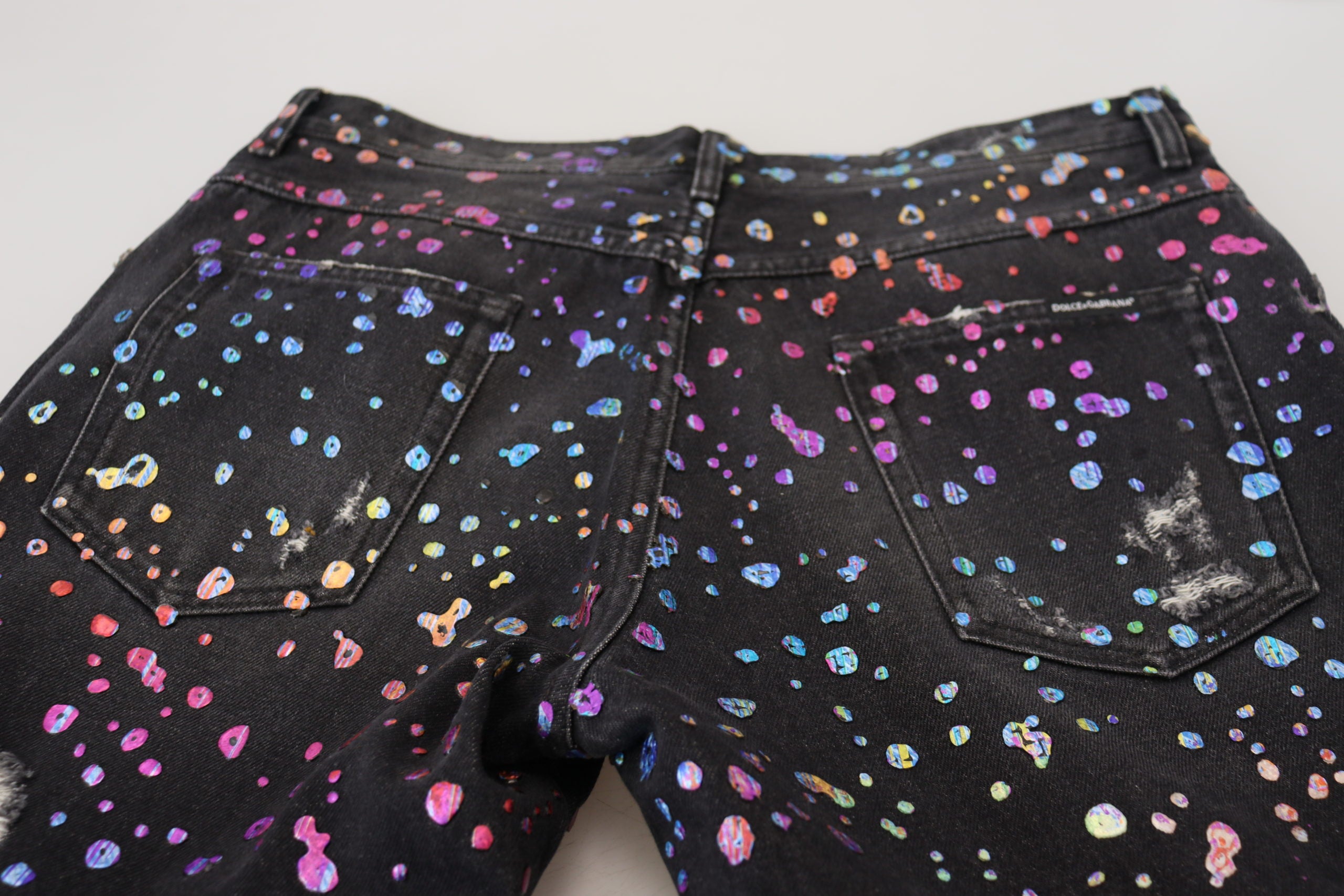 Black multicolor print tattered denim jeans by Dolce & Gabbana with distressed details and vibrant pattern, displayed on a plain background.