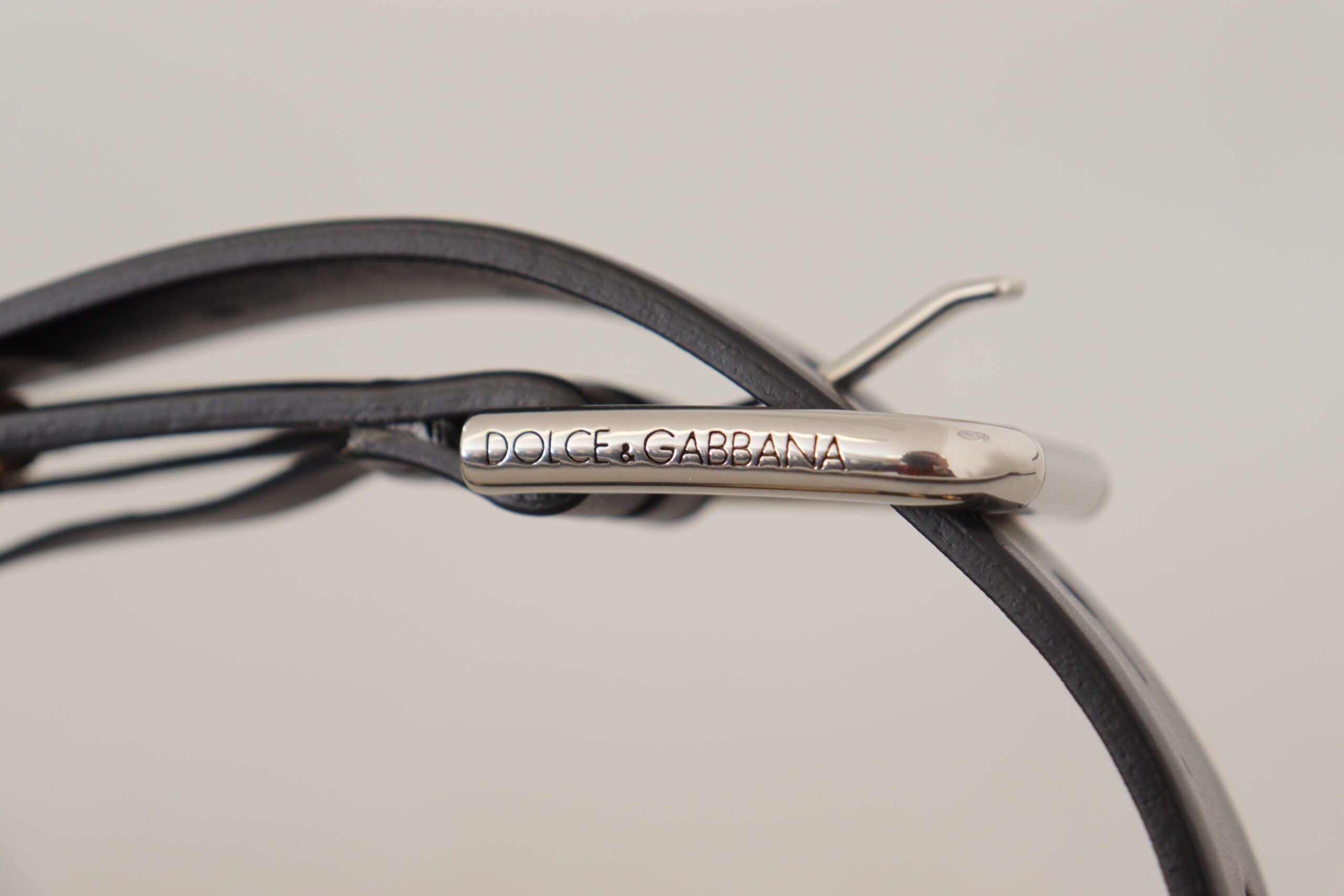 Black leather belt with eyelet details and silver tone metal buckle from Dolce & Gabbana, shown with a close-up of the buckle.