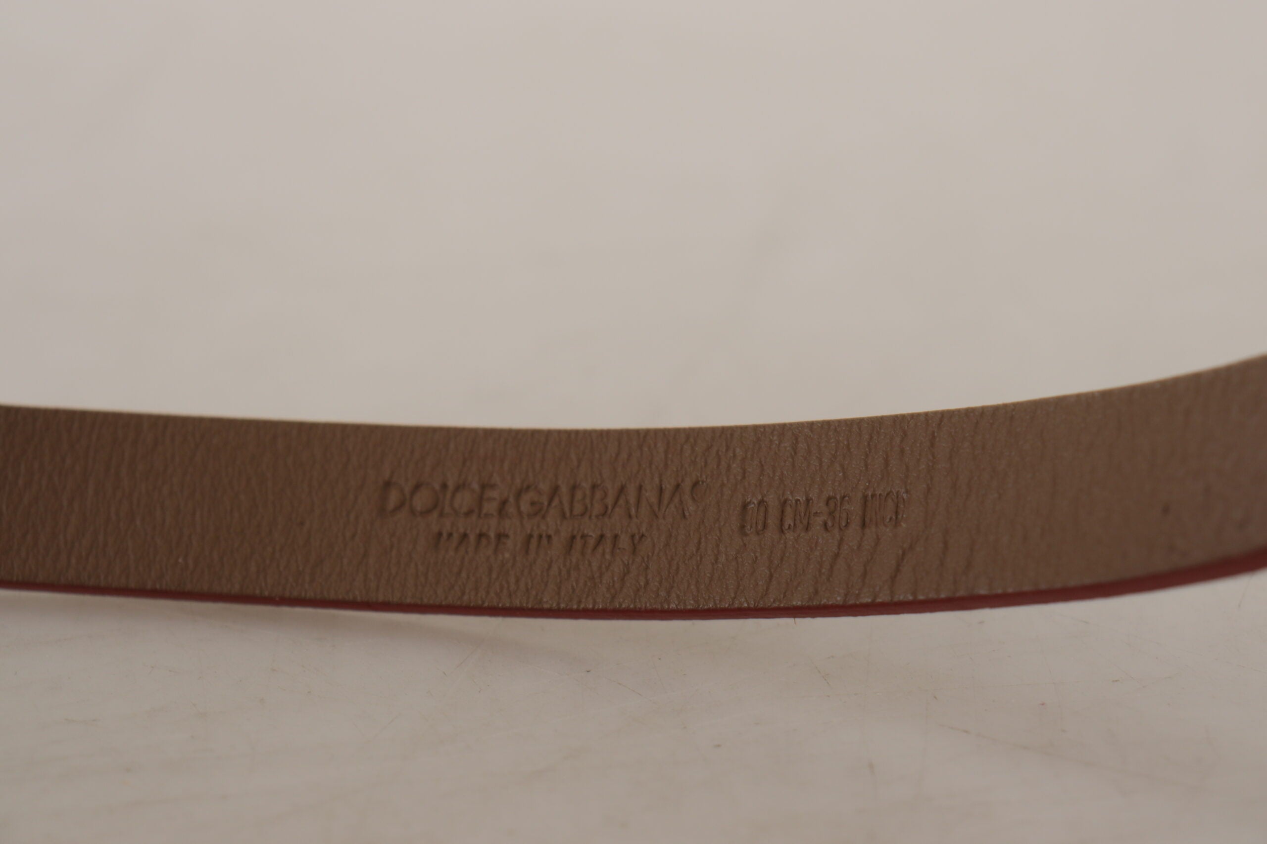 Brown leather belt with engraved metal waist buckle featuring Dolce & Gabbana logo and detailing.