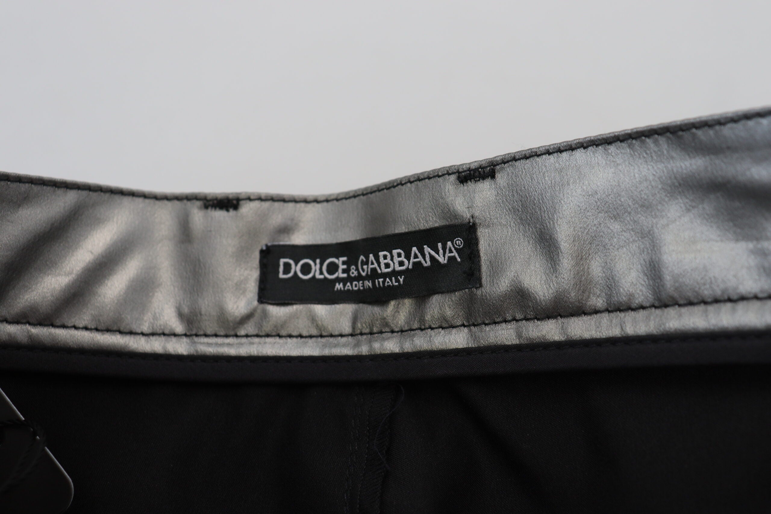 Metallic silver high-waist skinny pants by Dolce & Gabbana, shown on a model with a close-up of the shiny fabric and fitted style.