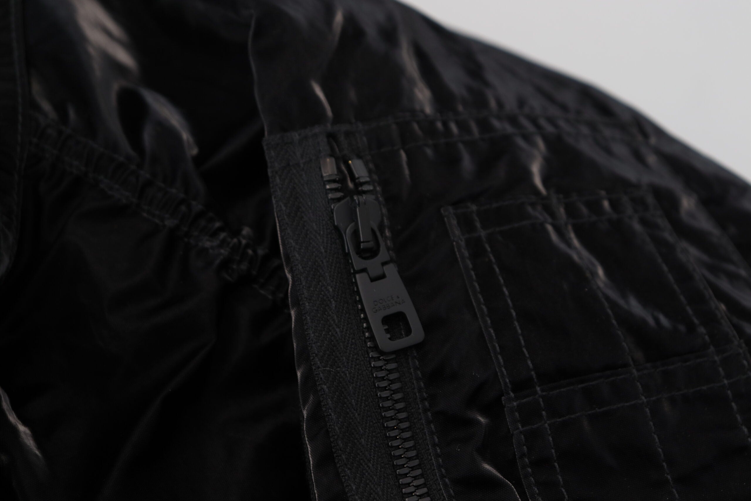 Black nylon hooded full zip bomber jacket by Dolce & Gabbana, shown with adjustable hood, front zipper, and ribbed cuffs.