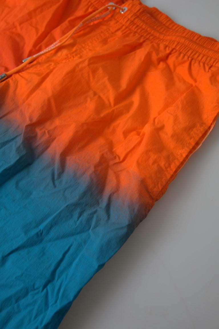 Dolce & Gabbana orange and blue gradient beachwear swimwear shorts displayed on a model for summer poolside fashion.