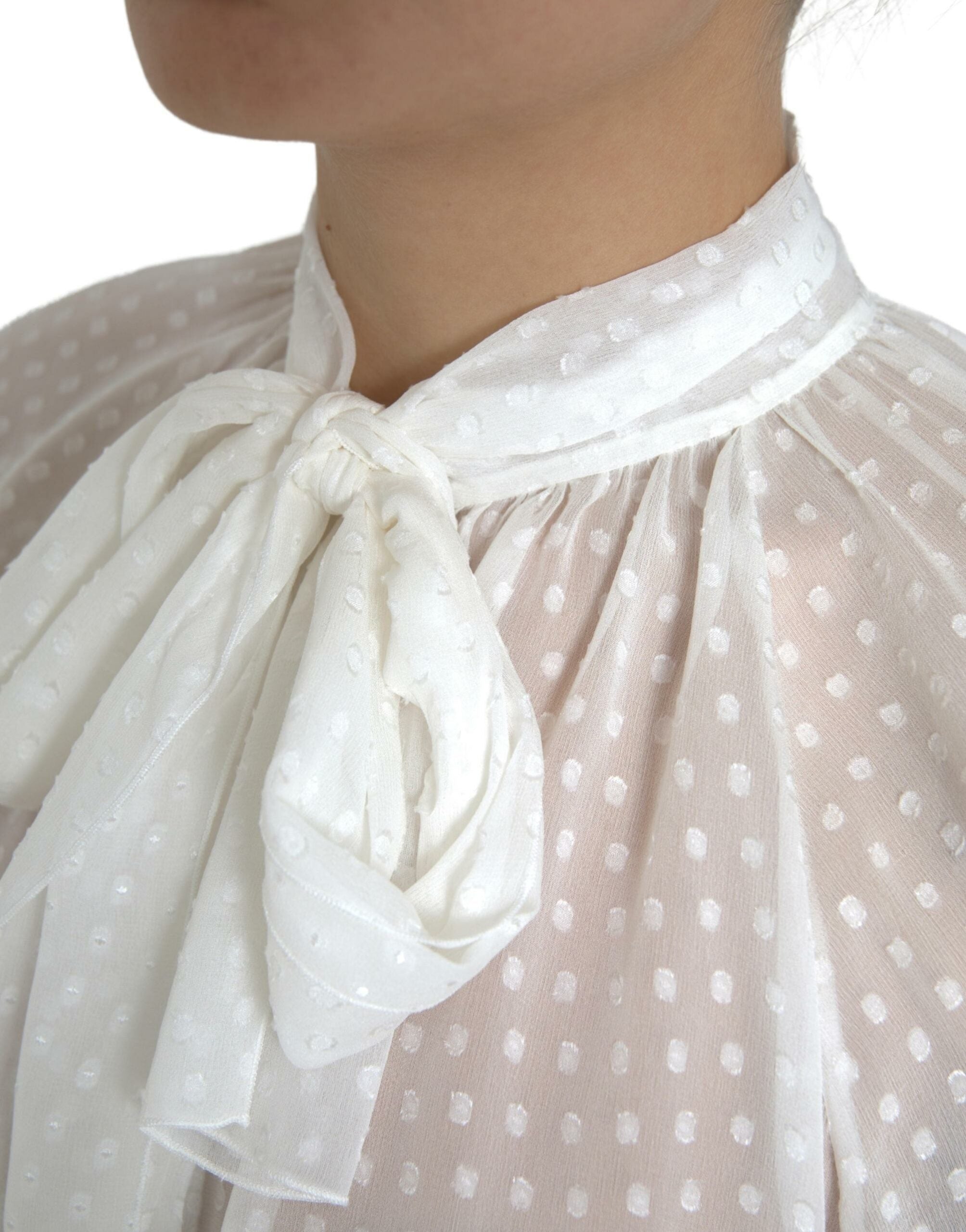 White silk sheer blouse with tied neck and polka dot pattern by Dolce & Gabbana, shown on a model.