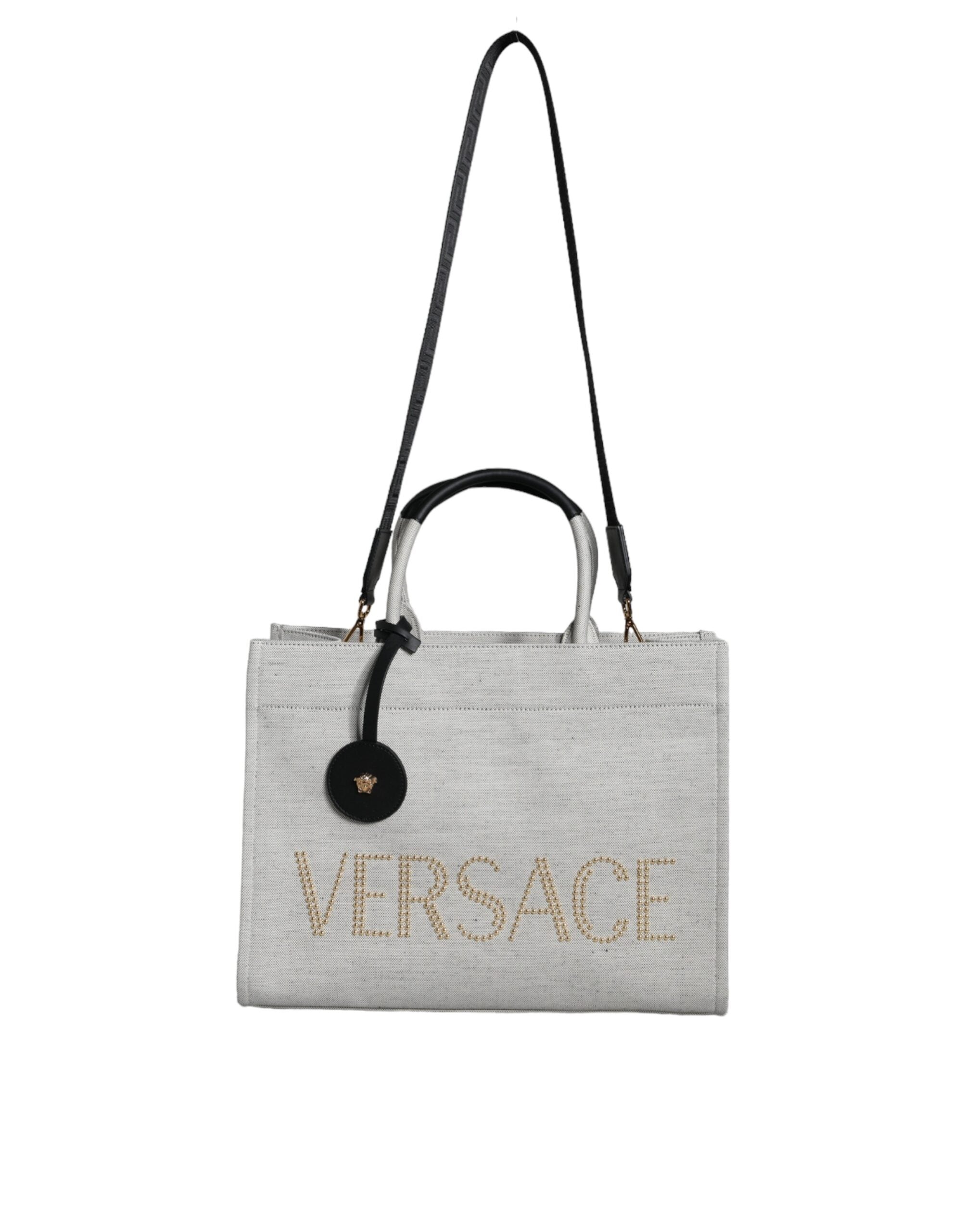 White Versace crossbody tote bag with top handles, canvas and leather construction, featuring the brand logo and spacious interior.