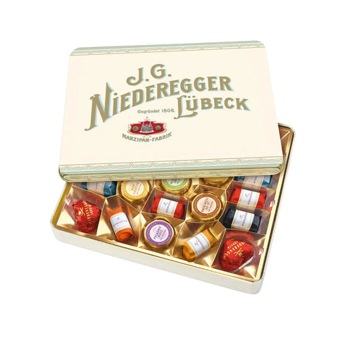 Assorted marzipan treats from Jag Couture London-New York inside a Nostalgia tin, displayed with colorful marzipan pieces and decorative packaging.